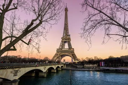 A stunning view of the Eiffel Tower silhouetted against a vibrant sunset sky, with shades of orange, pink, and purple reflecting off the clouds and illuminating the Paris skyline.